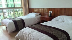 A hotel room with two beds, a wooden headboard, a nightstand with a kettle, and a view of a balcony with a railing. - Guxiangqing Hotel (Wuyuan)