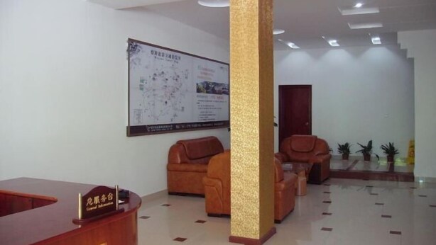 A reception area with a wooden reception desk, leather sofas, a large map on the wall, and a staircase in the background. - Guxiangqing Hotel (Wuyuan)
