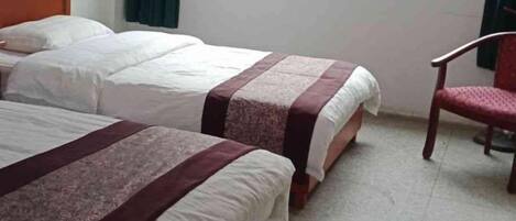 Una habitación con dos camas, una silla y un ventanal.