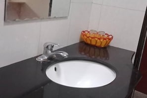 Ein Badezimmer mit schwarzem Waschtisch, weißem Waschbecken und einem Glasbehälter mit orangefarbenen Griffen.