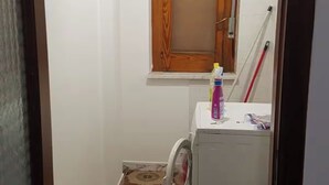 Una lavanderia con lavatrice, scopa e finestra con stipite in legno.