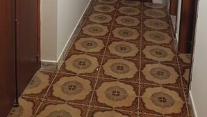 Un corridoio con piastrelle decorate, una porta in legno con un vetrino e un lampadario al soffitto.