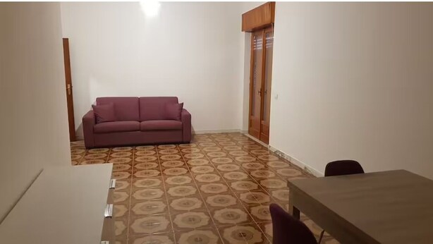 Una stanza con un pavimento a motivi, una porta in legno, un divano viola e un tavolo.