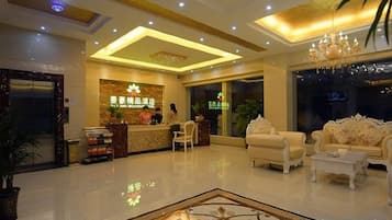 A hotel lobby with a reception desk, seating area, and a chandelier.