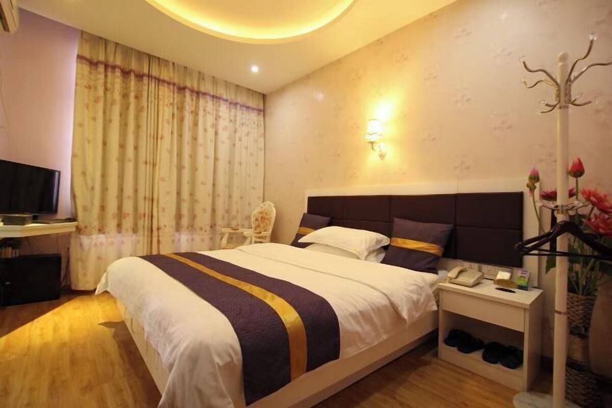 Quarto de hotel com cama, mesa de cabeceira, abajur e televisão.