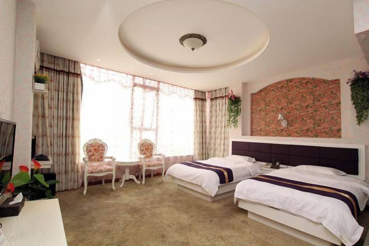Quarto de hotel com duas camas, uma mesinha, uma cadeira e uma televisão.