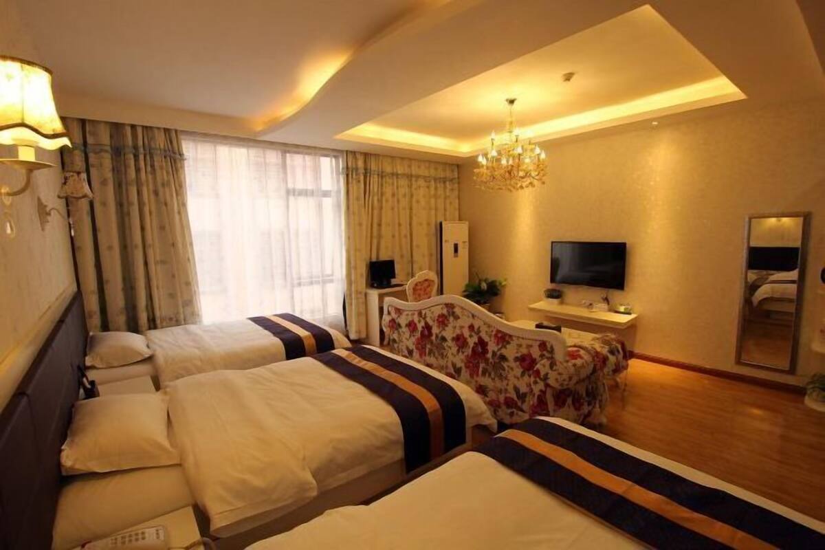 Quarto de hotel com duas camas, televisão, escrivaninha, espelho e um candelabro.