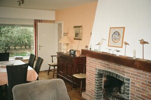 A cozy room with a brick fireplace, a dining table with chairs, a lamp, and a framed picture of birds. - Beautiful villa in a quiet environment close to the beach (Koksijde)