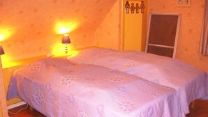 Une chambre avec deux lits, un plancher en bois, une lampe fixée au mur et une porte avec une fenêtre.