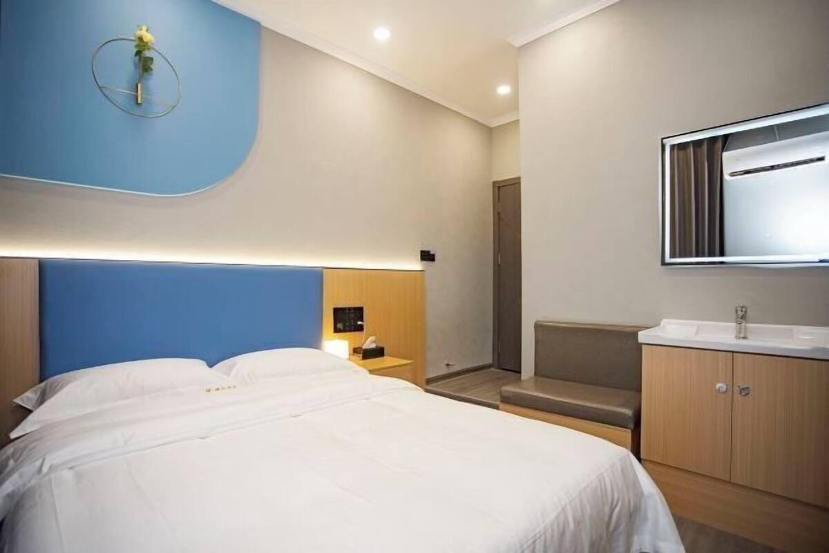Quarto de hotel moderno com uma cama grande, uma mesinha de cabeceira, um espelho e um banco embutido.