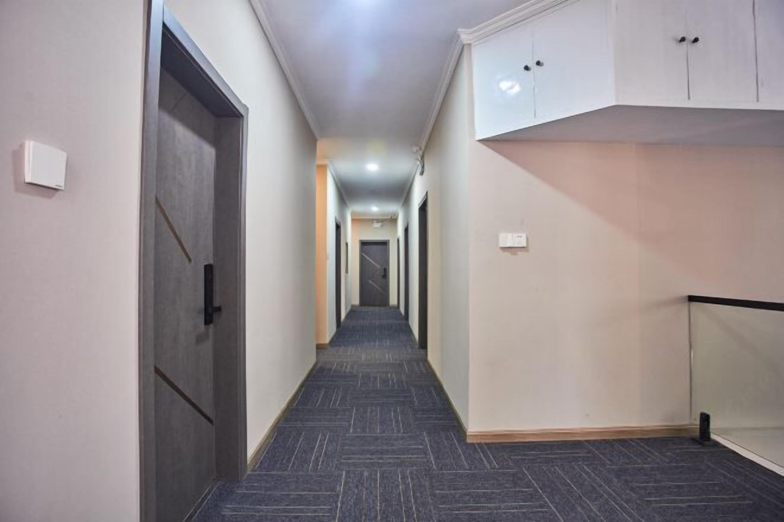 Un pasillo estrecho con piso alfombrado, una puerta a la izquierda y una barandilla de cristal a la derecha.