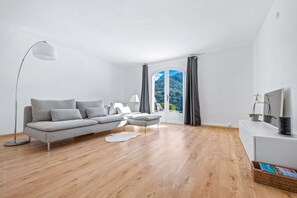 A modern living room with a grey sofa, a floor lamp, a white rug, and a view of mountains through a glass door.