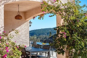 An outdoor dining area with a table and chairs, a hanging light fixture, and a view of a forested hill. - Luxury Villa 8w/ Pool, Sea &amp; Mountain Views (Fréjus)