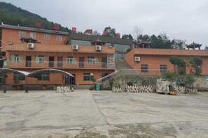 A multi-story building with a central staircase, a covered outdoor area, and a stone wall with plants. - Junlong Holiday Hotel (Dafang)