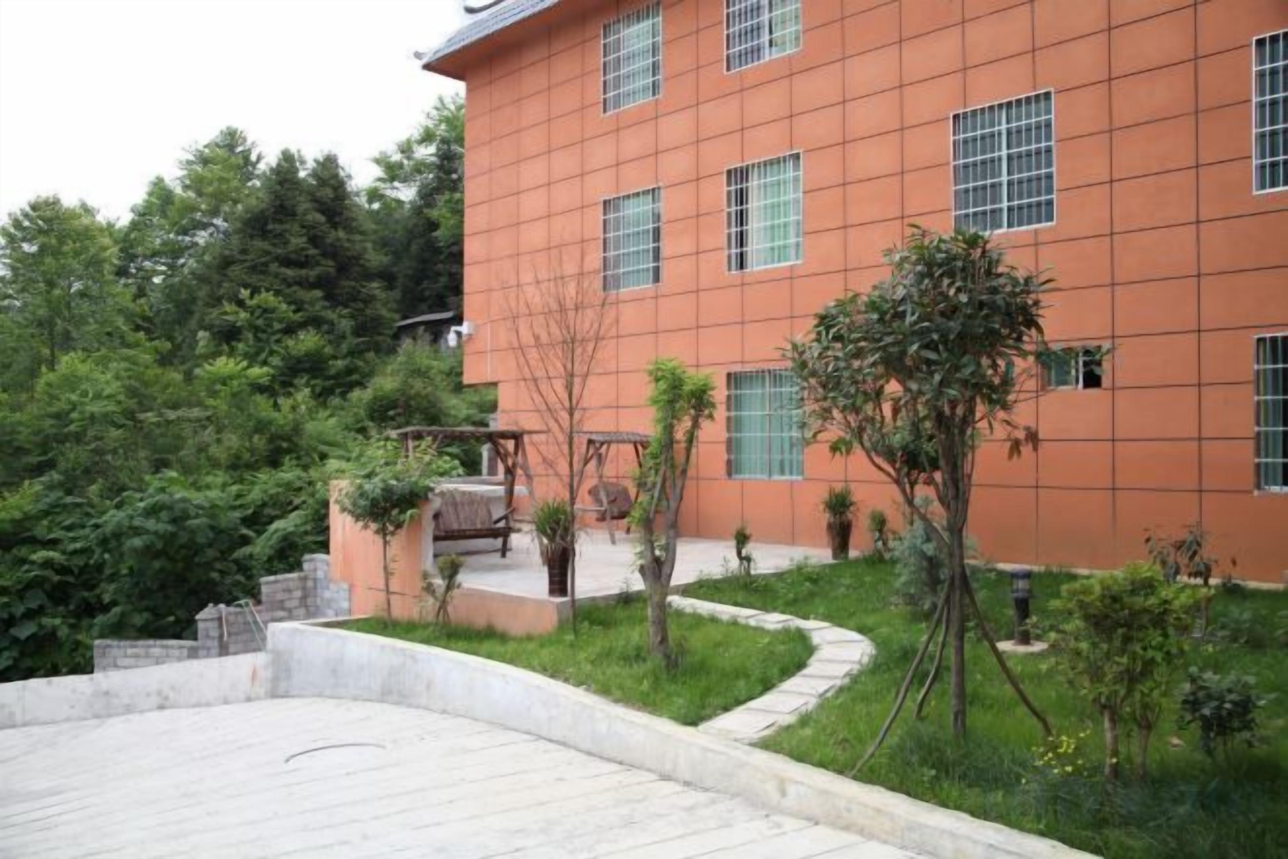 A building with a red facade, multiple windows, and a landscaped garden area with trees and a pathway.