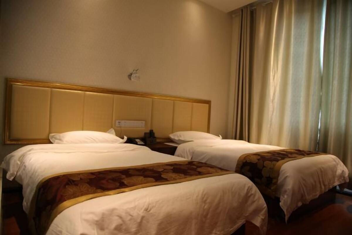 Two single beds with headboards and pillows, dressed in white linens and a floral bedspread, are set against a neutral backdrop.