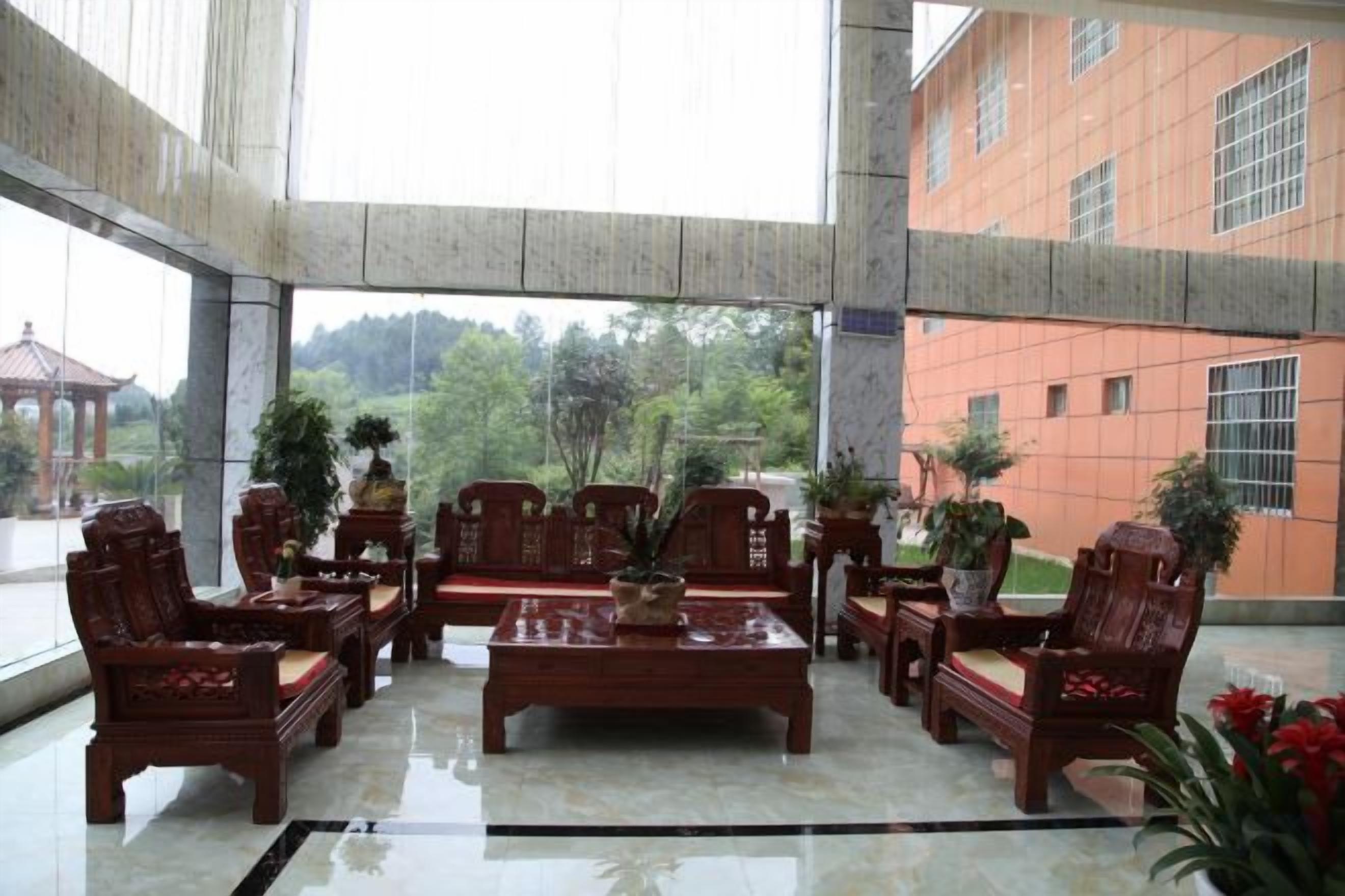 A lobby with a high ceiling, a central coffee table surrounded by chairs, and a view of a building and trees outside.