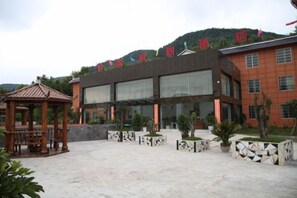 A building with a flat roof, large windows, and a paved courtyard with a gazebo. - Junlong Holiday Hotel (Dafang)