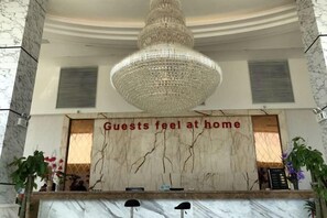 A reception desk with a marble top, a chandelier above, and a sign that reads 'Guests feel at home'. - Junlong Holiday Hotel (Dafang)