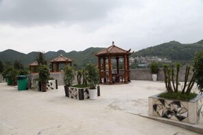 A rooftop terrace with potted plants, wooden gazebos, and a view of a mountainous landscape. - Junlong Holiday Hotel (Dafang)