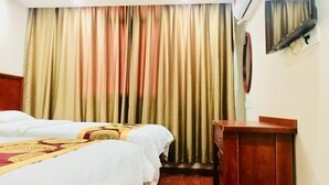 Camera d'albergo con due letti, una scrivania in legno e un'ampia finestra con tende.