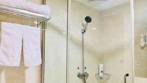 Cabina doccia in vetro, soffione a mano, portasci con asciugamani e dispenser di sapone su un ripiano.