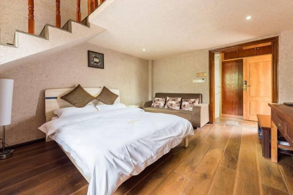 A bedroom with a bed, a nightstand, a dresser, a lamp, and a staircase.