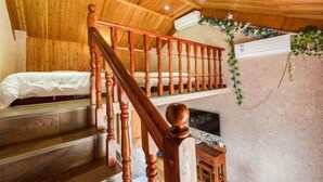 Una escalera de madera lleva a un dormitorio en un altillo con una cama y un televisor.