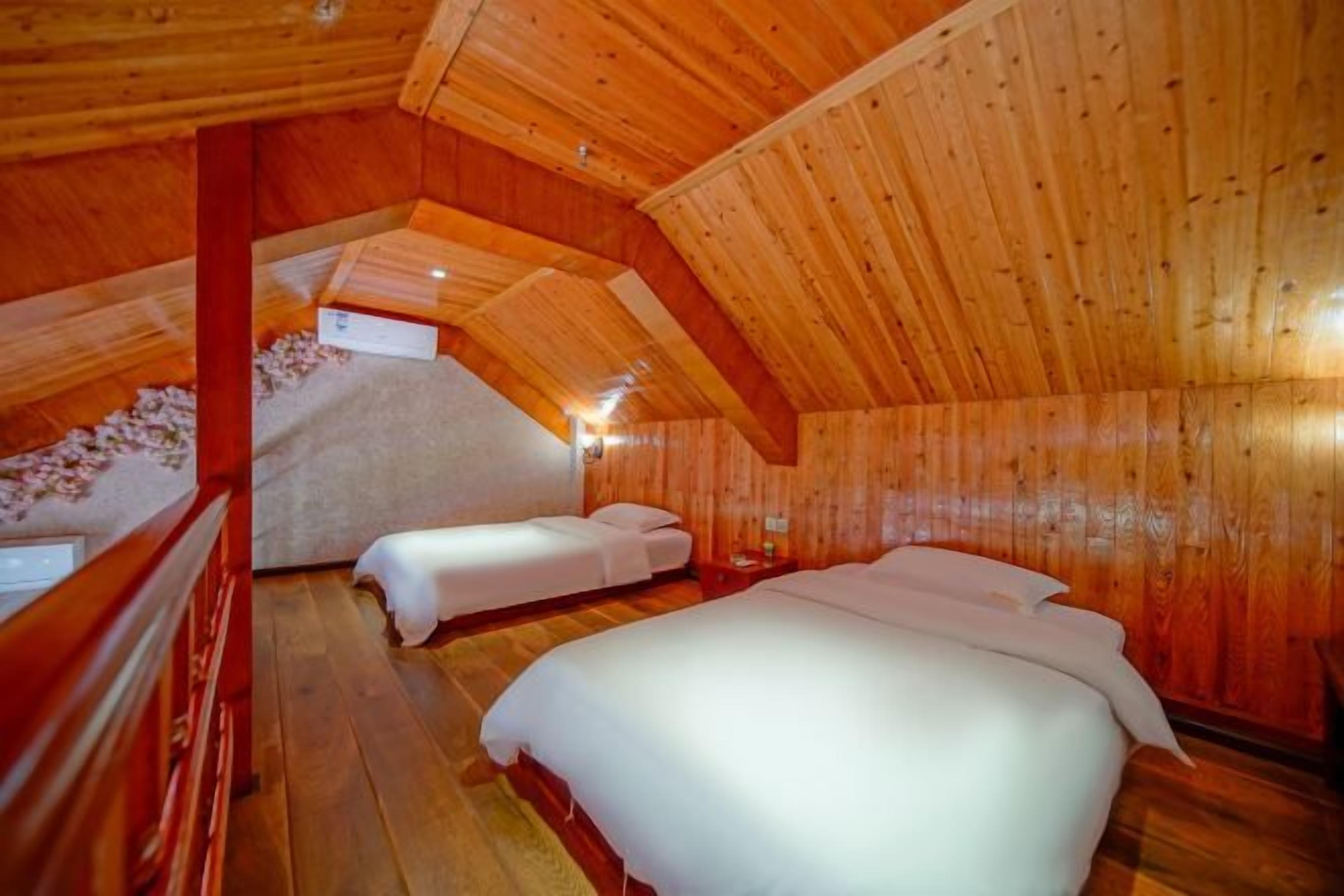 Un interior de madera con dos camas, techo de madera y una pequeña mesa.