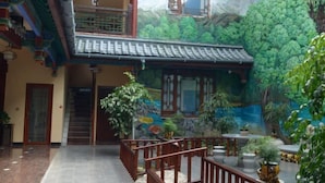 Un edificio tradicional con un mural que representa un paisaje boscoso, una escalera de madera y un balcón con barandillas.