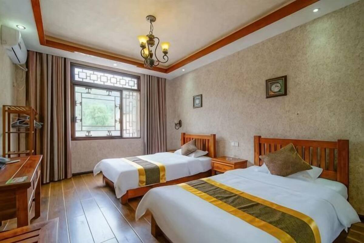 A hotel room with two beds, a desk, a chair, a window with curtains, and a chandelier.