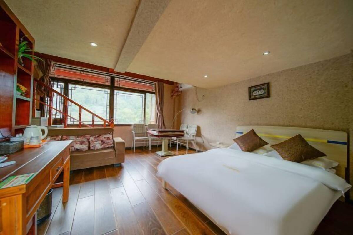 A hotel room with a bed, a desk, a chair, a small table, and a window with a view.