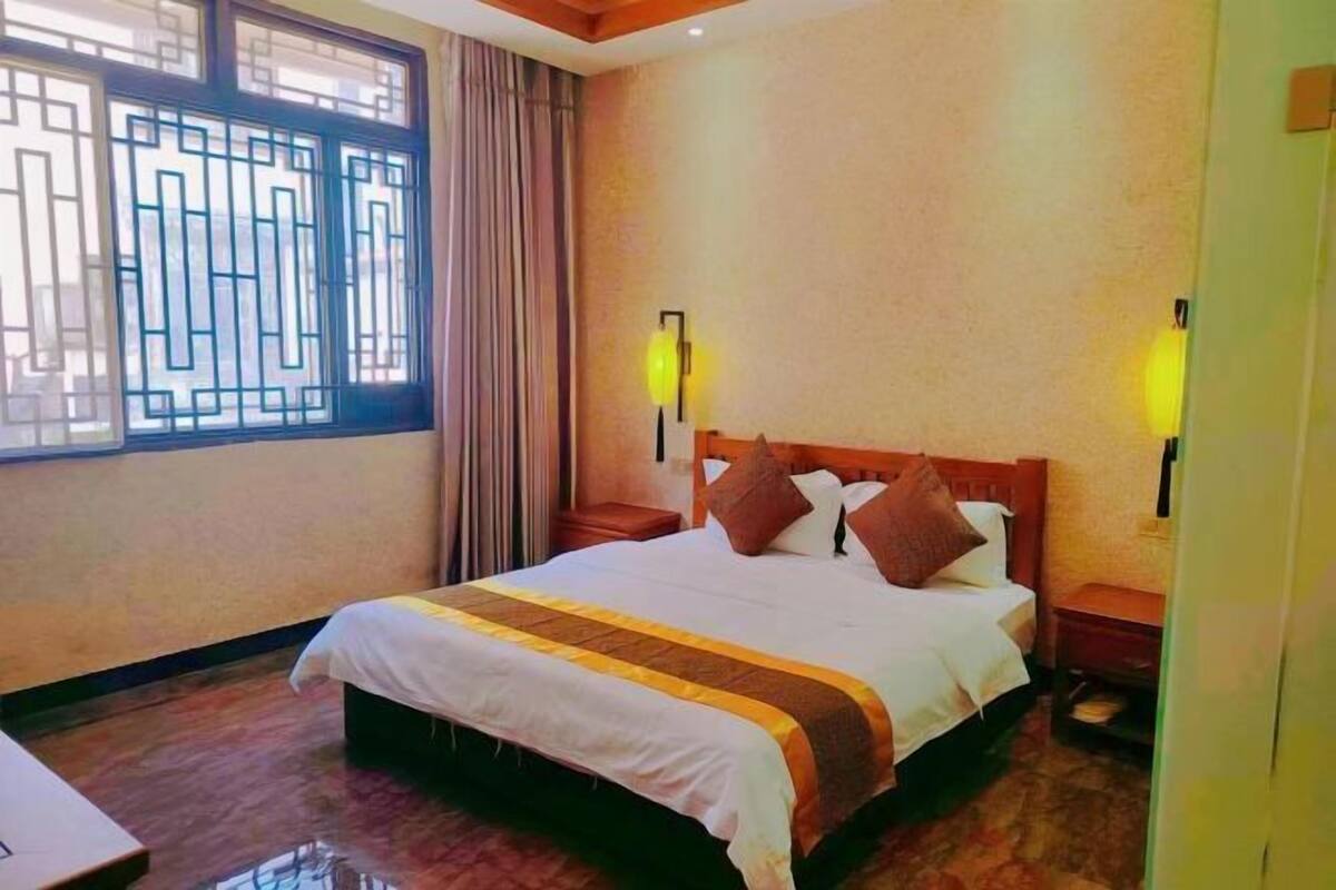 A hotel room with a large bed, two bedside tables, a window with decorative grills, and wall-mounted lamps.