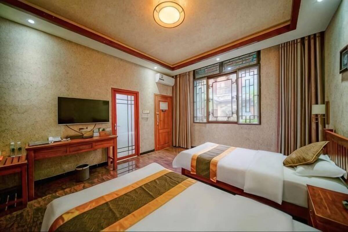 A hotel room with two beds, a desk with a TV, a window with curtains, and a door.