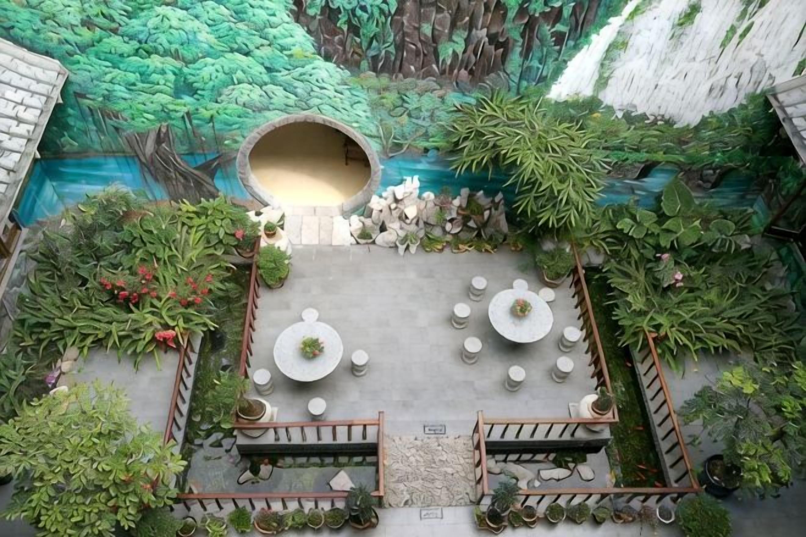 An outdoor seating area with tables and chairs, surrounded by potted plants and a mural.