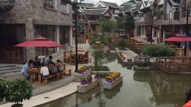 Un patio tradicional con edificios de piedra, muebles de madera y una fuente central.