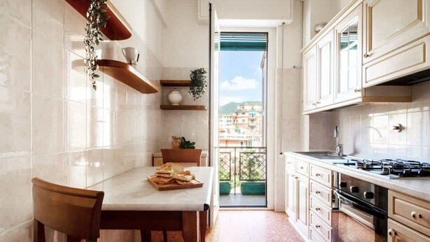 A kitchen with white cabinets, a wooden table, and a view of buildings through a glass door. - OMAR'S HOUSE - Affitti Brevi Italia (Rapallo)