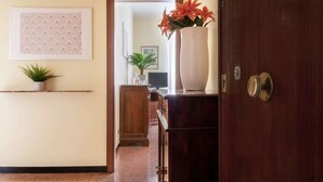A hallway with a wooden door, a potted plant, a framed picture, and a vase with flowers. - OMAR'S HOUSE - Affitti Brevi Italia (Rapallo)