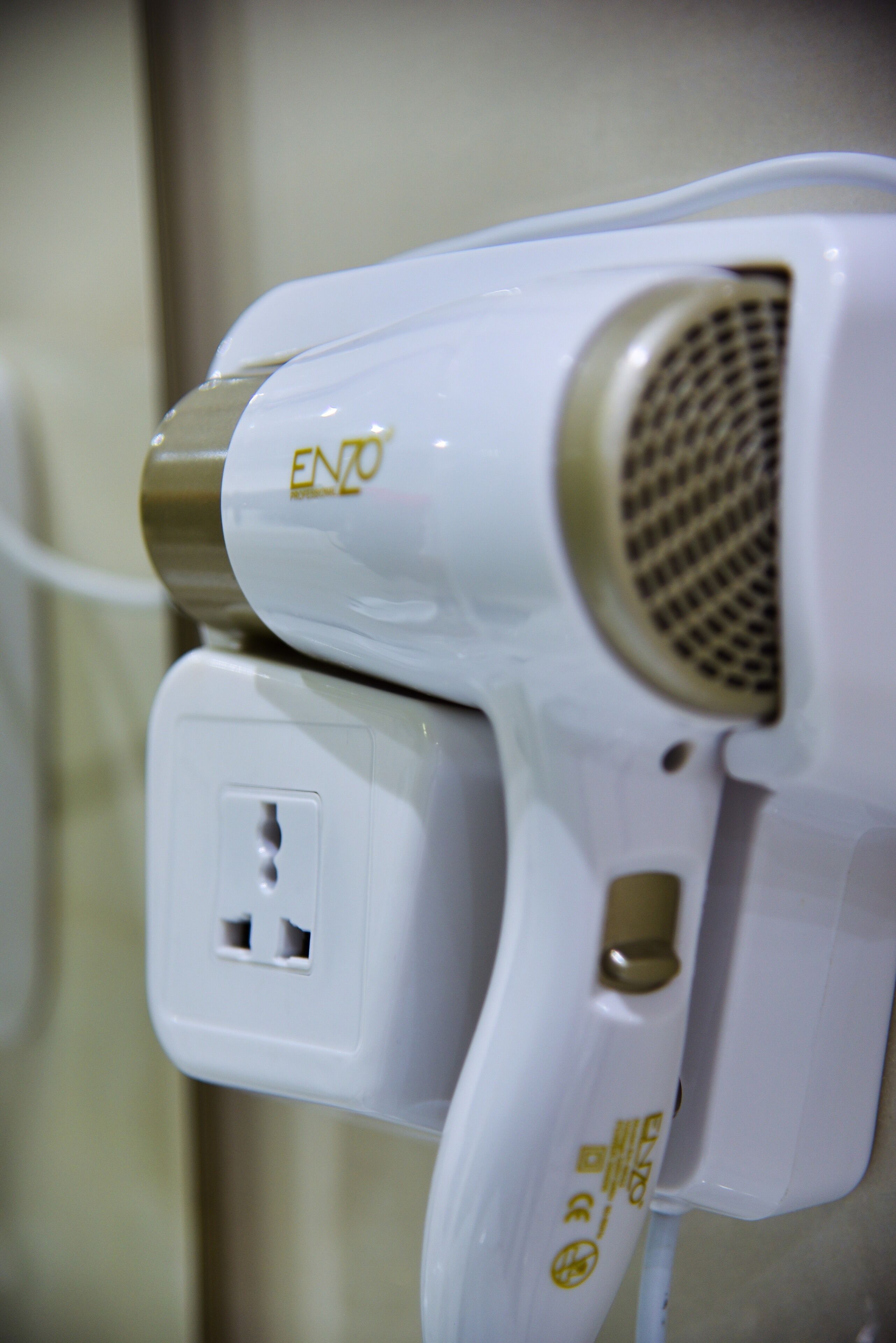 A white hair dryer with a gold accent and a power cord plugged in.