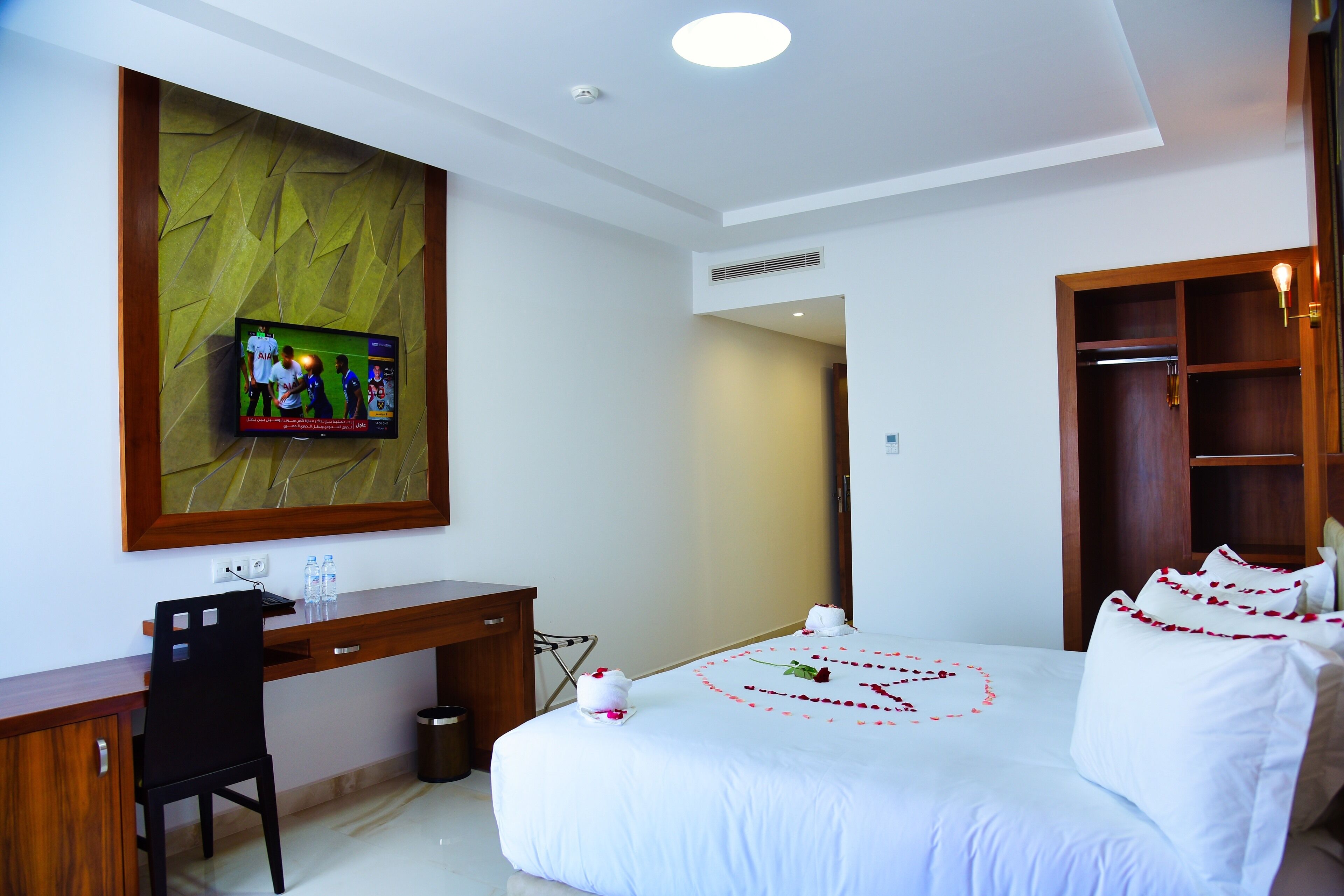 Habitación de hotel con cama, escritorio, televisor montado en una pared con textura y armario de madera.