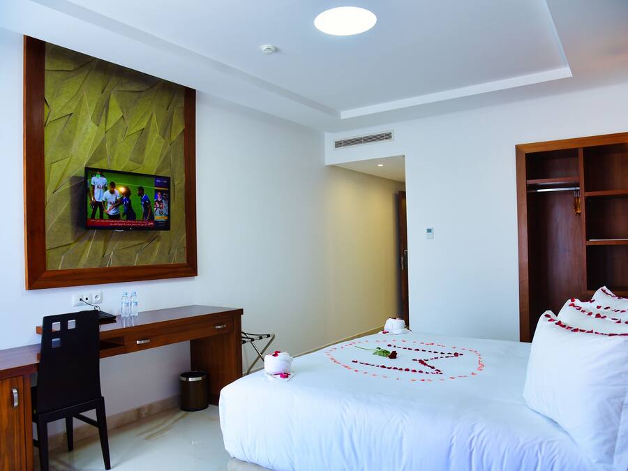 Habitación de hotel con cama, escritorio, televisor montado en una pared con textura y armario de madera.