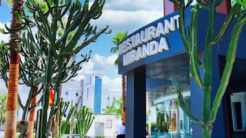 Un restaurante llamado 'RESTAURANT MIRANDA' con terraza, palmeras y un cielo azul despejado.