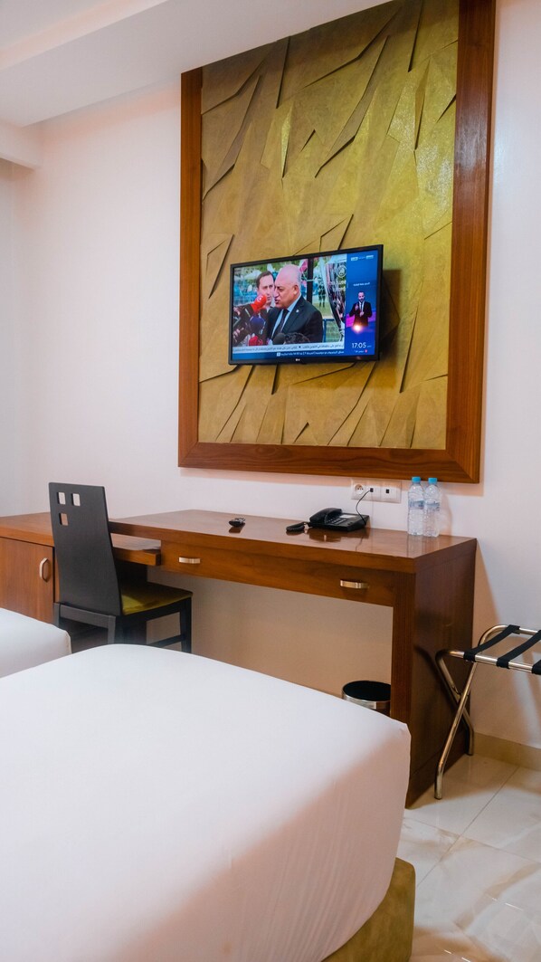 A hotel room with a TV mounted on the wall, a wooden desk, a chair, a bed, and a crutch leaning against the wall.