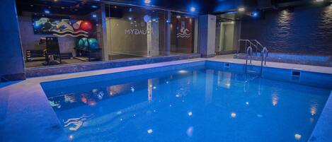 Una piscina interior con agua cristalina, un muro de cristal y un logotipo visible en la pared.