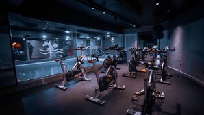 Un gimnasio con bicicletas estáticas, espejos y un muro de cristal.
