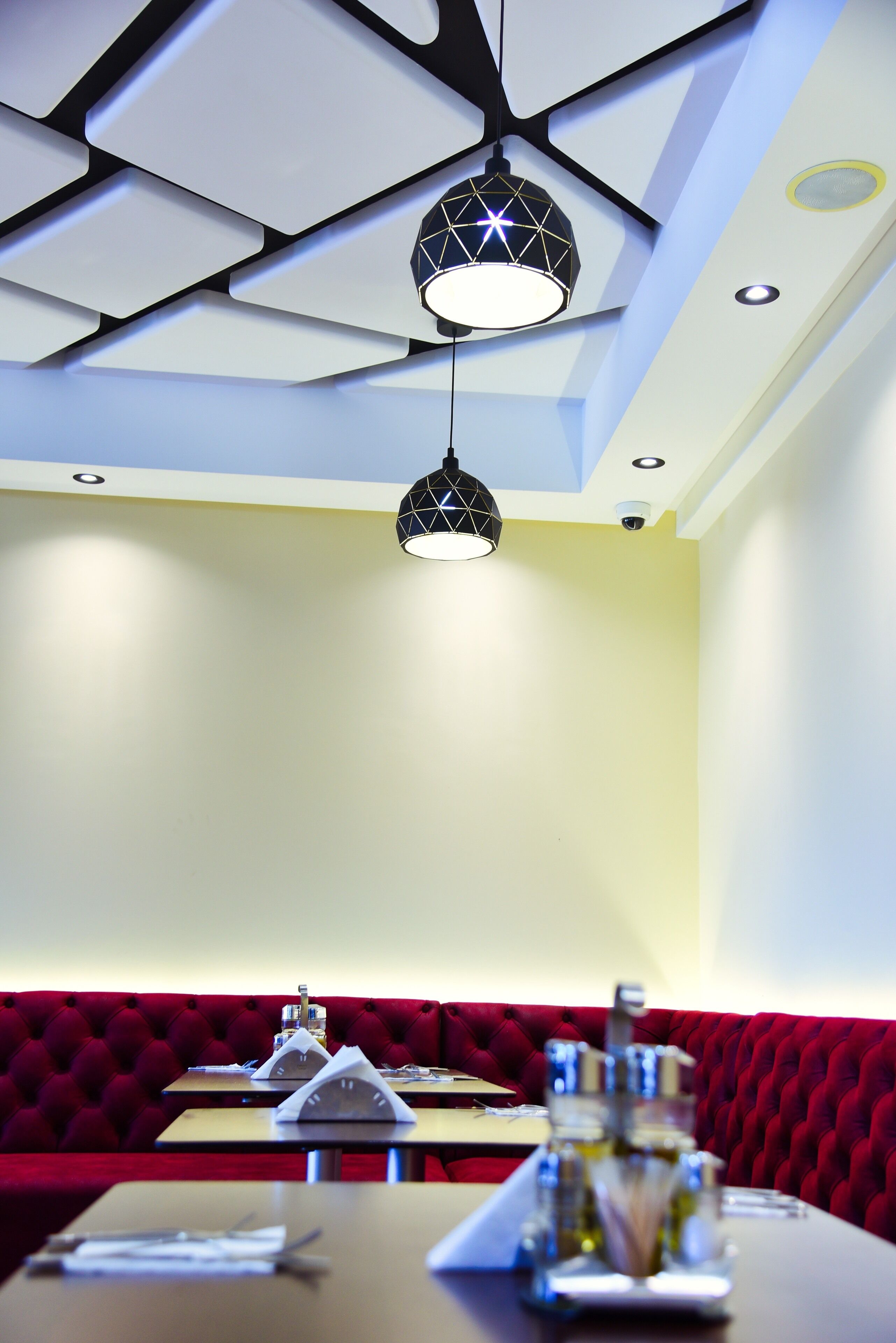 Interior de restaurante con un diseño moderno en el techo, cabinas de terciopelo rojo y mesas ordenadas con servilletas y cubiertos.