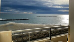 Un balcon avec vue sur une plage, une digue rocheuse et l’océan.