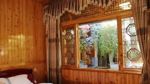 Une pièce en bois avec un lit, une fenêtre ornée de grilles métalliques décoratives et une vue sur la verdure à l’extérieur.