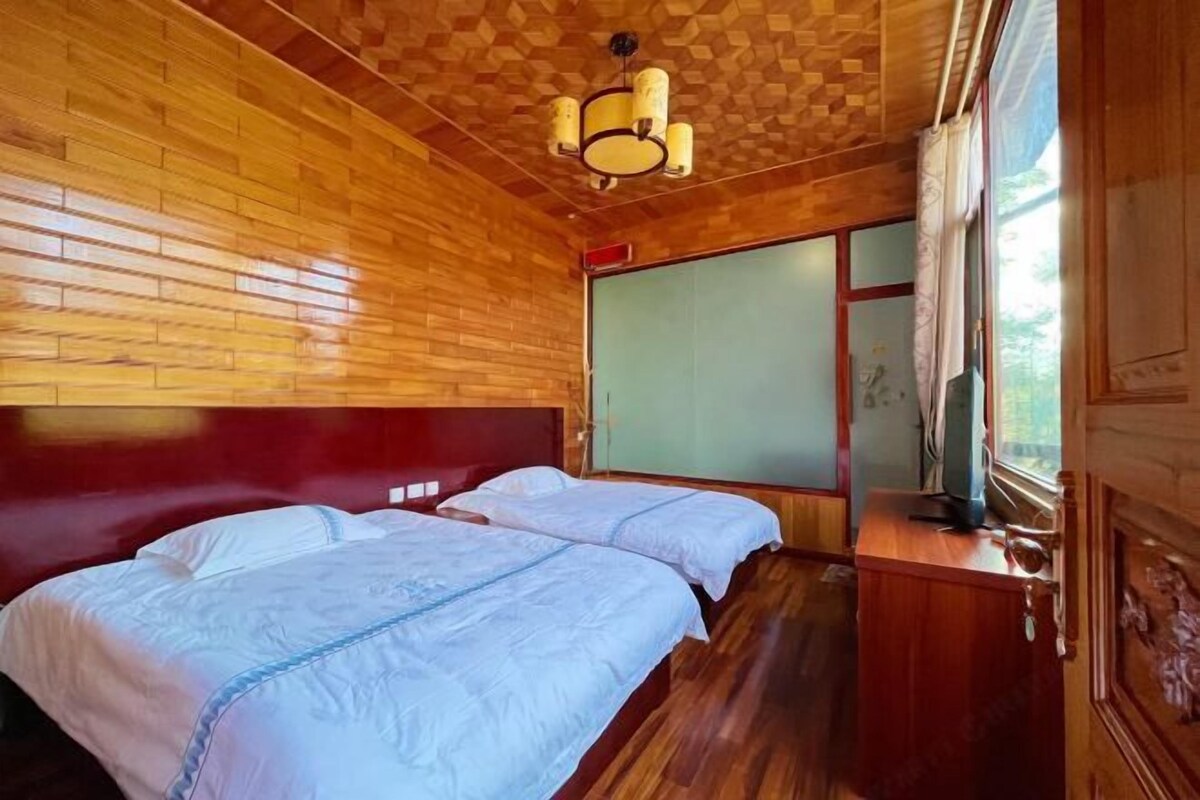 A wooden-paneled room with two beds, a wooden desk, and a window with curtains.