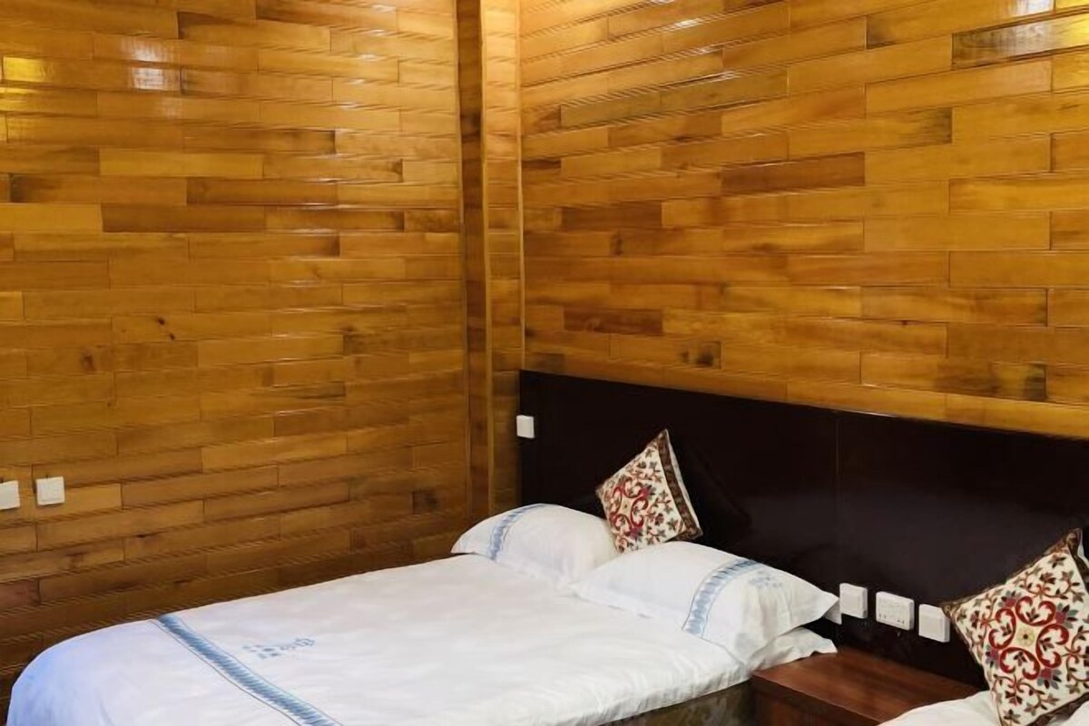 Una habitación con paneles de madera, una cama con ropa blanca y almohadas estampadas, y un cabecero oscuro.